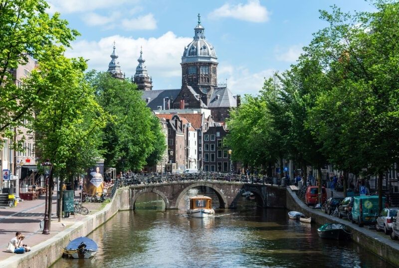 Amsterdam canal with a stone bridge, trees, bicycles, and historic buildings